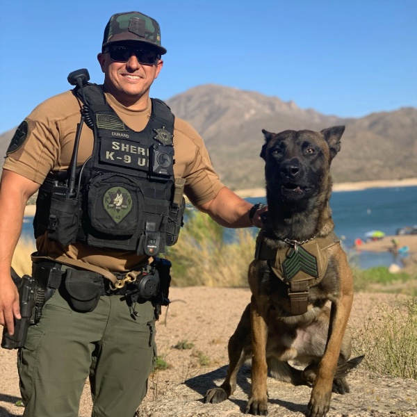 Deputy Durand kneeling beside his K9 with a desert lake behind them
